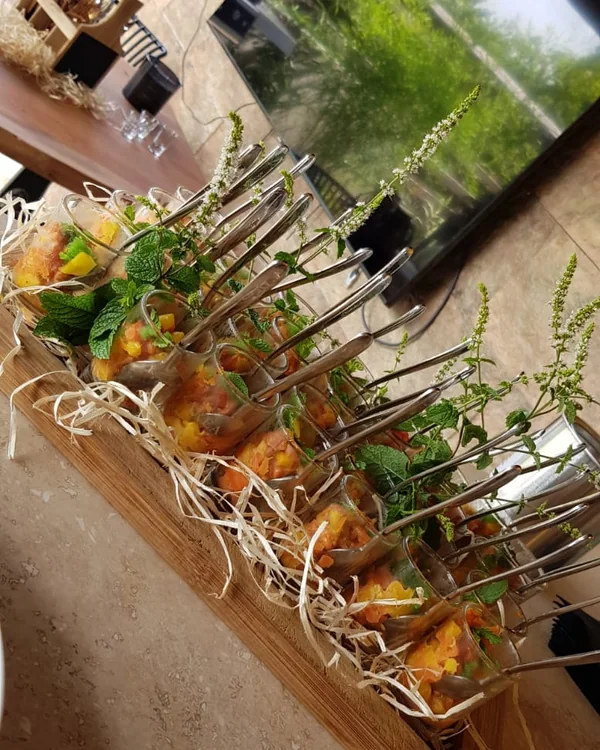 A long wooden board of tartare glasses set in straw and decorated with flowering mint